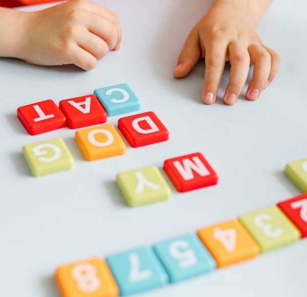 A child's hand arranging magnetic letters  to form words. This illustrate the process of letter sound.