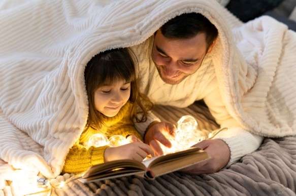 Father and child reading with a flashlight under a blanket.