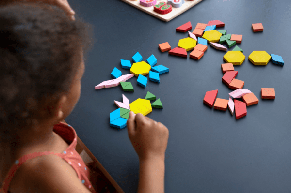 A child surrounded by objects of different shapes on the table.