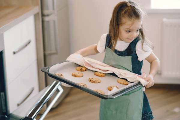 Child removing chocolate chips cookies from the oven to count them during a baking session.