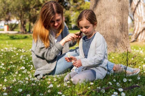 Preschooler outdoors counting flower petals with her mother as a way to make math fun and Interactive