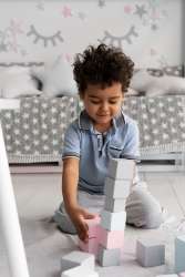 : A smiling preschooler with two piles of blocks, one larger and one smaller as he understands the concept of more and less.