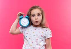 Young child holding an alarm clock that she uses to learn basic time concepts.