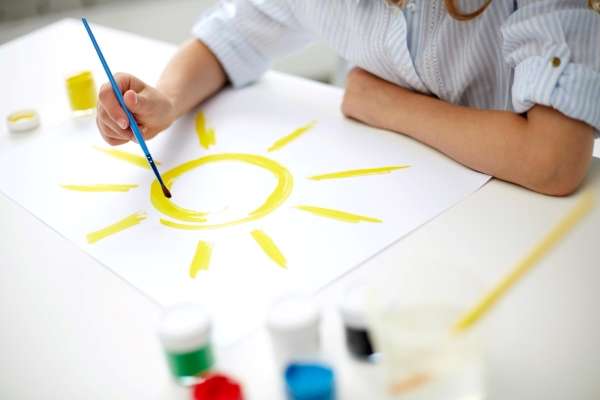 A child painting an image of sun on a piece of paper as a way to understand basic geometry concepts