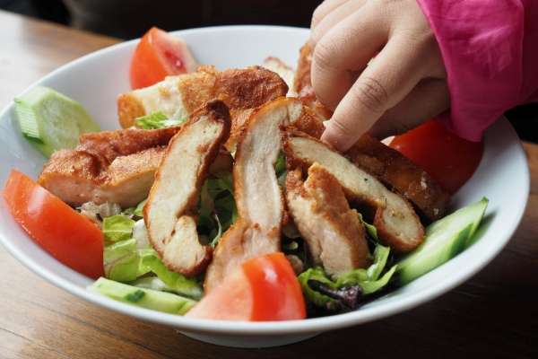 Child's hand picking a piece of grilled chicken.