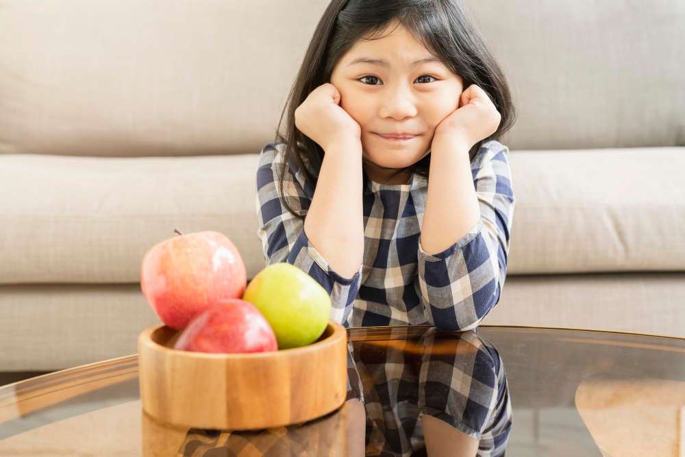  A child smiling at a bowl of apples on the table to use to understand basic number operations.