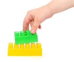 Child's hand holding two different sizes of building blocks to learn greater than and less than concepts.