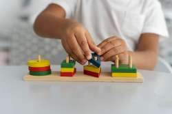 The child's hands sorting blocks of different colors and shapes to understand basic geometry concepts.