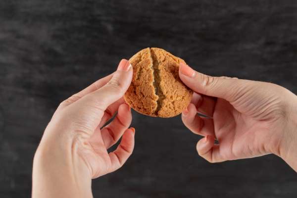 Close up of a hand cutting a cookie into half. Sharing is a good way to teach basic decimals concepts.