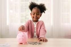 A child putting coins in a piggy bank. This is the best way to teach basic money concepts.