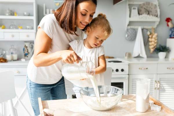 Child and parent in the kitchen measuring flour.