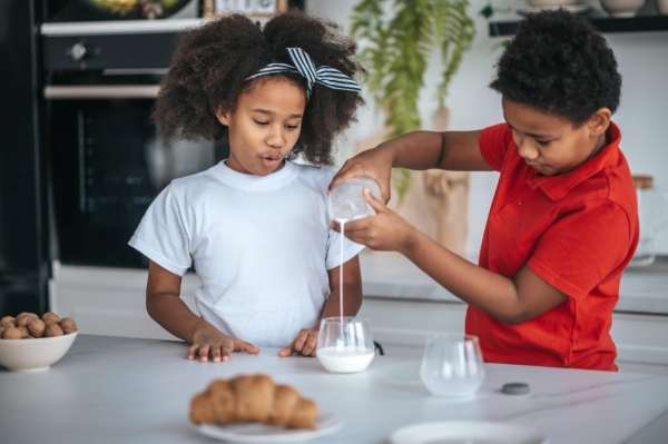 Two children measuring milk in a glass.