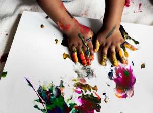 Child's hands covered in colorful washable paint ready to paint on a canvas learning how to How-to-finger paint using washable paint