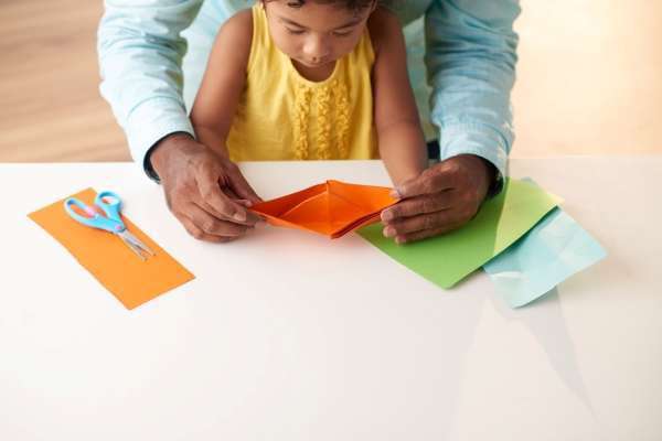 Proud preschooler showing off an origami boat.